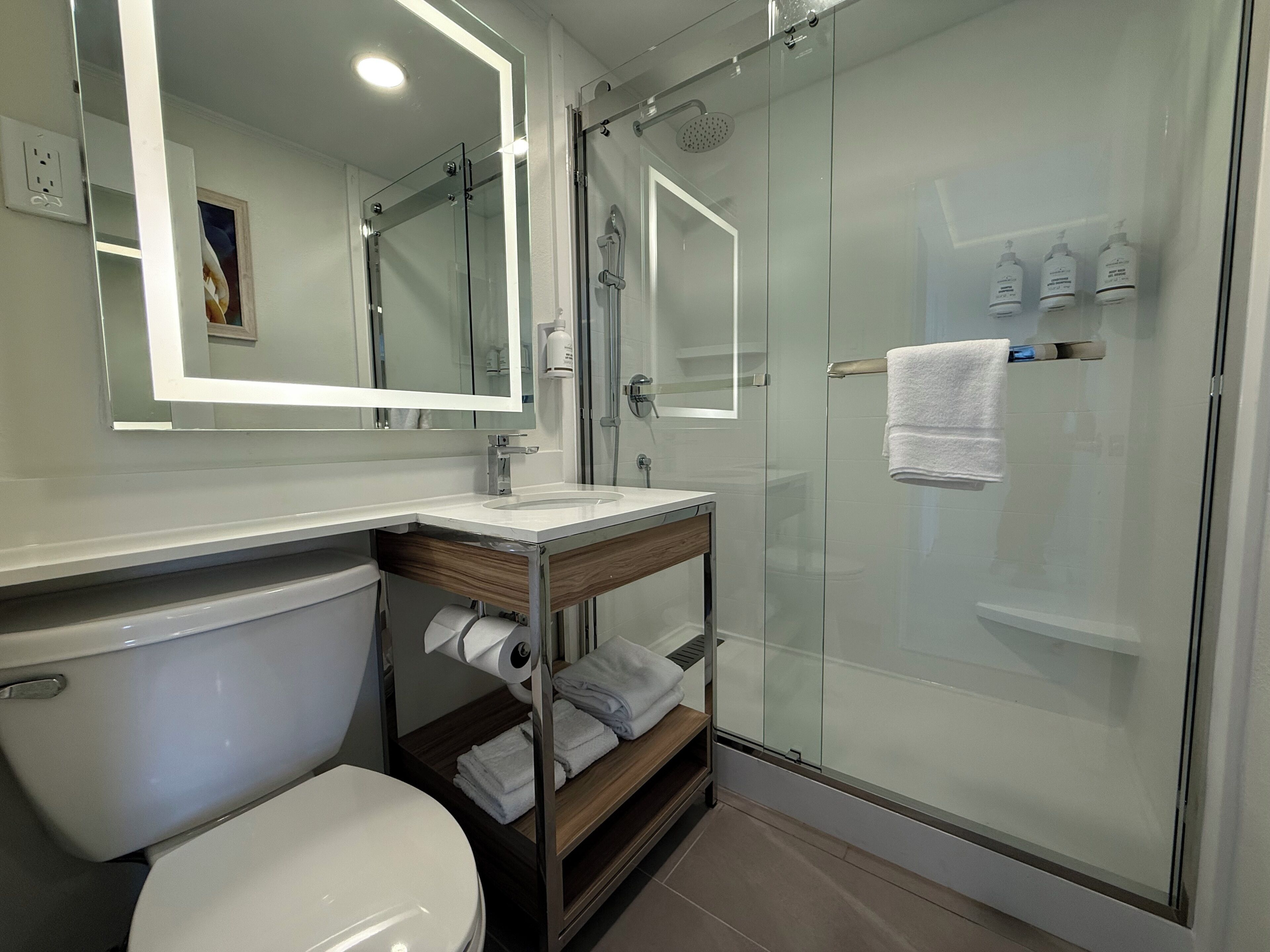Un baño moderno con ducha de vidrio, inodoro blanco y tocador con espejo y toallero.