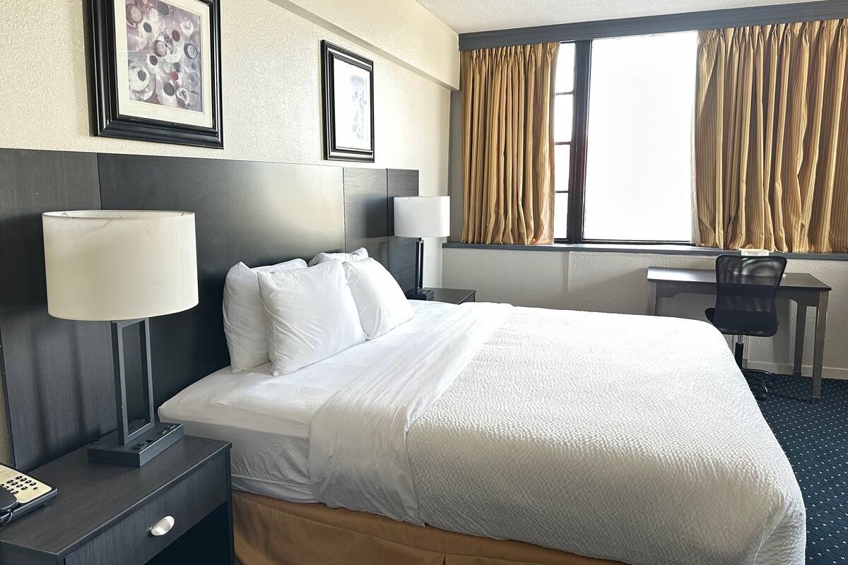 A hotel room with a bed, bedside lamps, a desk, and a chair.