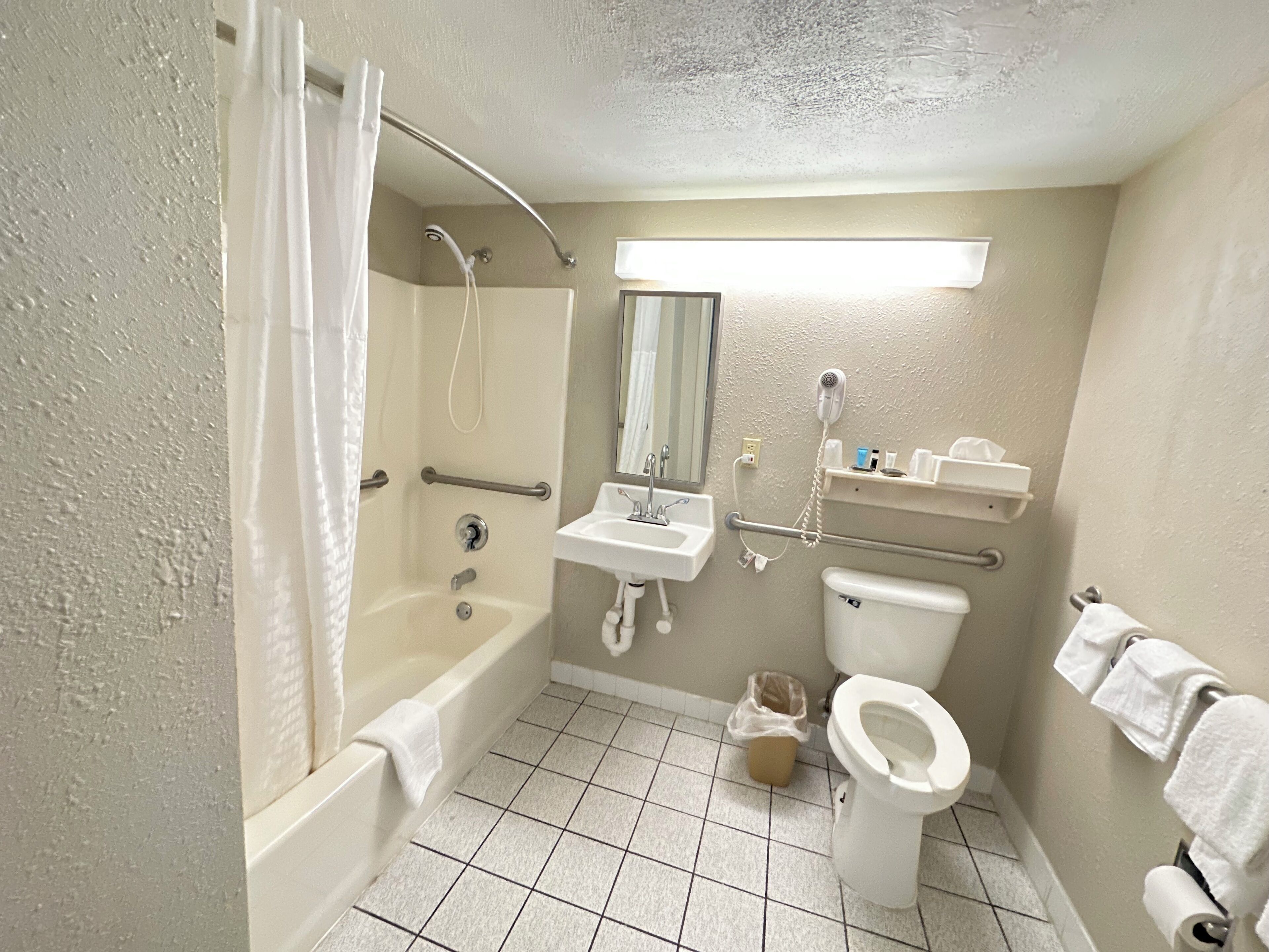 A bathroom with a bathtub, shower, sink, toilet, and hand dryer.