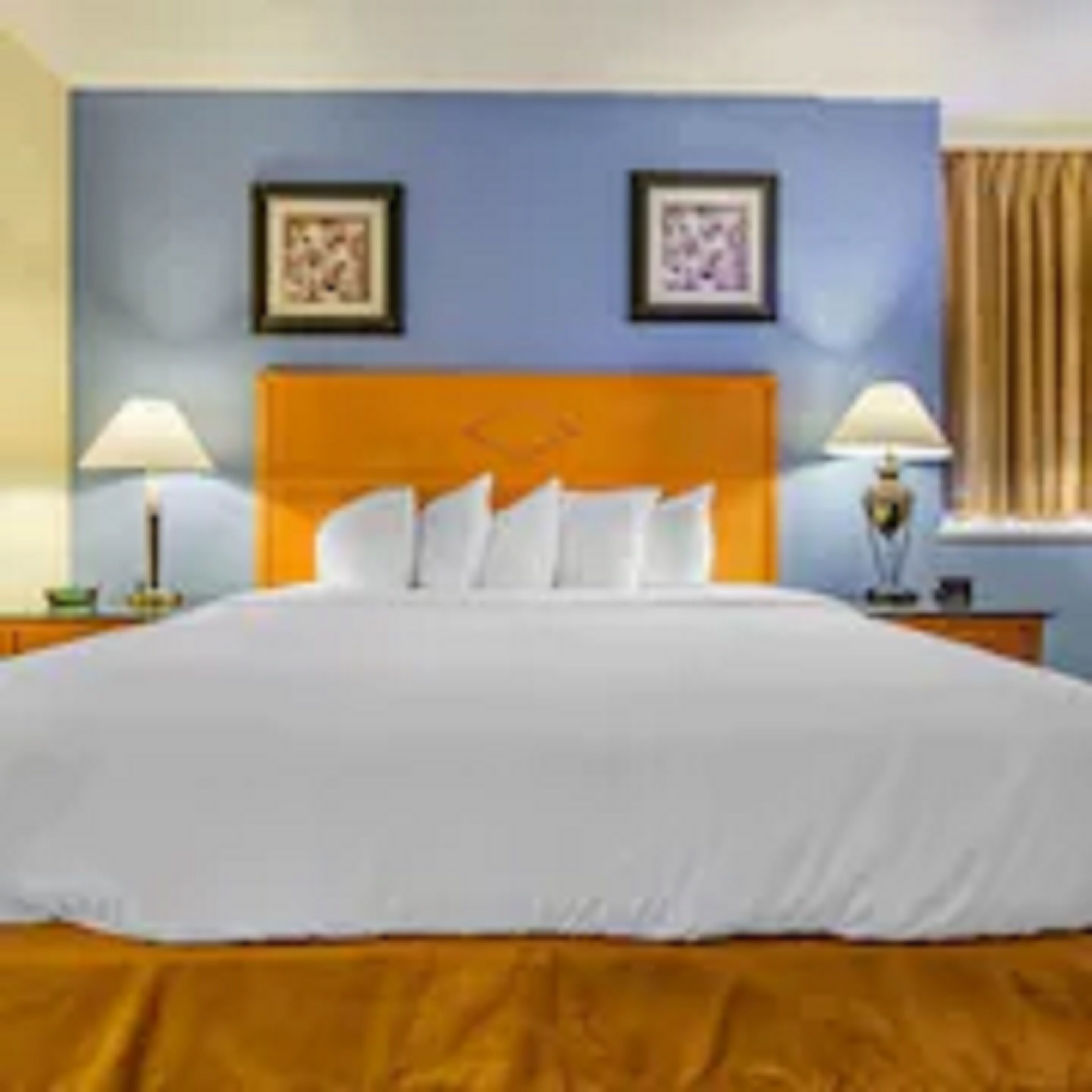 A hotel room with a large bed, two bedside tables with lamps, and two framed pictures on the wall.