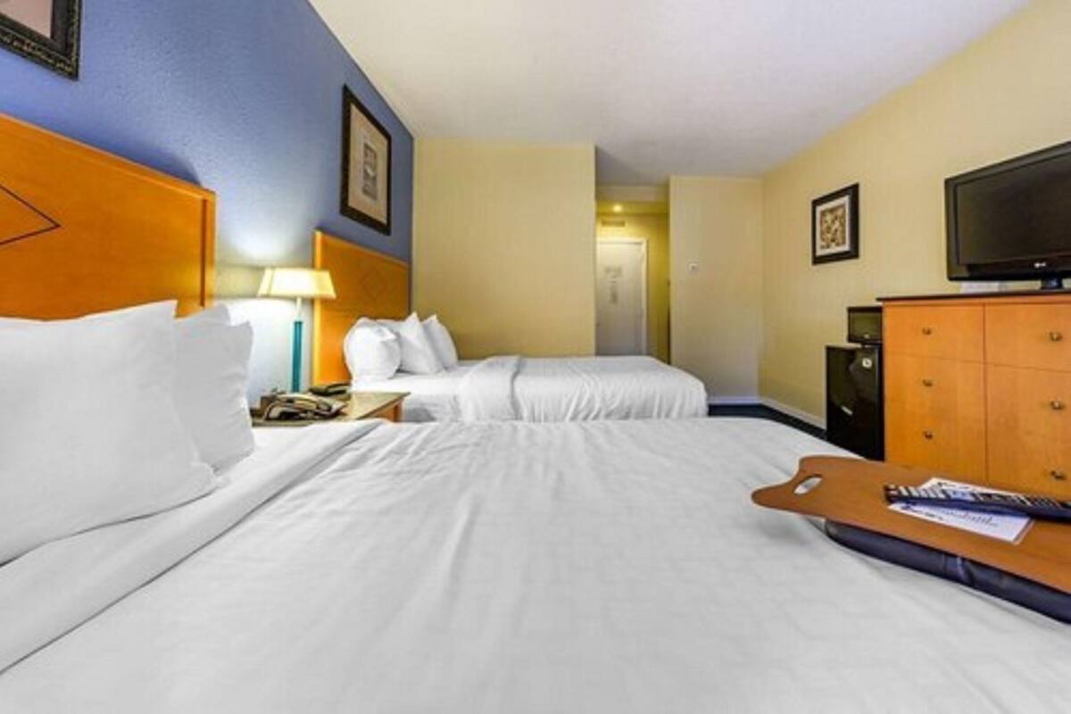 A hotel room with two beds, a TV, a desk, and a lamp.