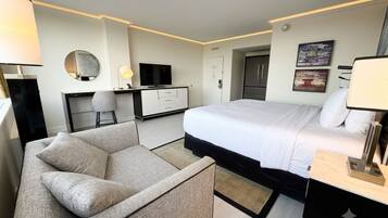 A modern hotel room with a bed, a desk, a chair, a TV, and a wardrobe.