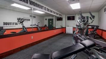 Una palestra con attrezzature per esercizi, un grande specchio e citazioni motivazionali alle pareti.