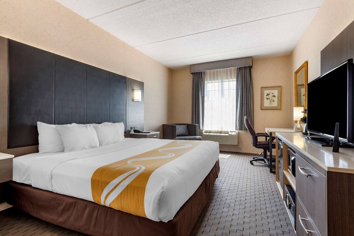 Une chambre d’hôtel avec un grand lit, un bureau avec une télévision, une chaise et une fenêtre avec des rideaux.