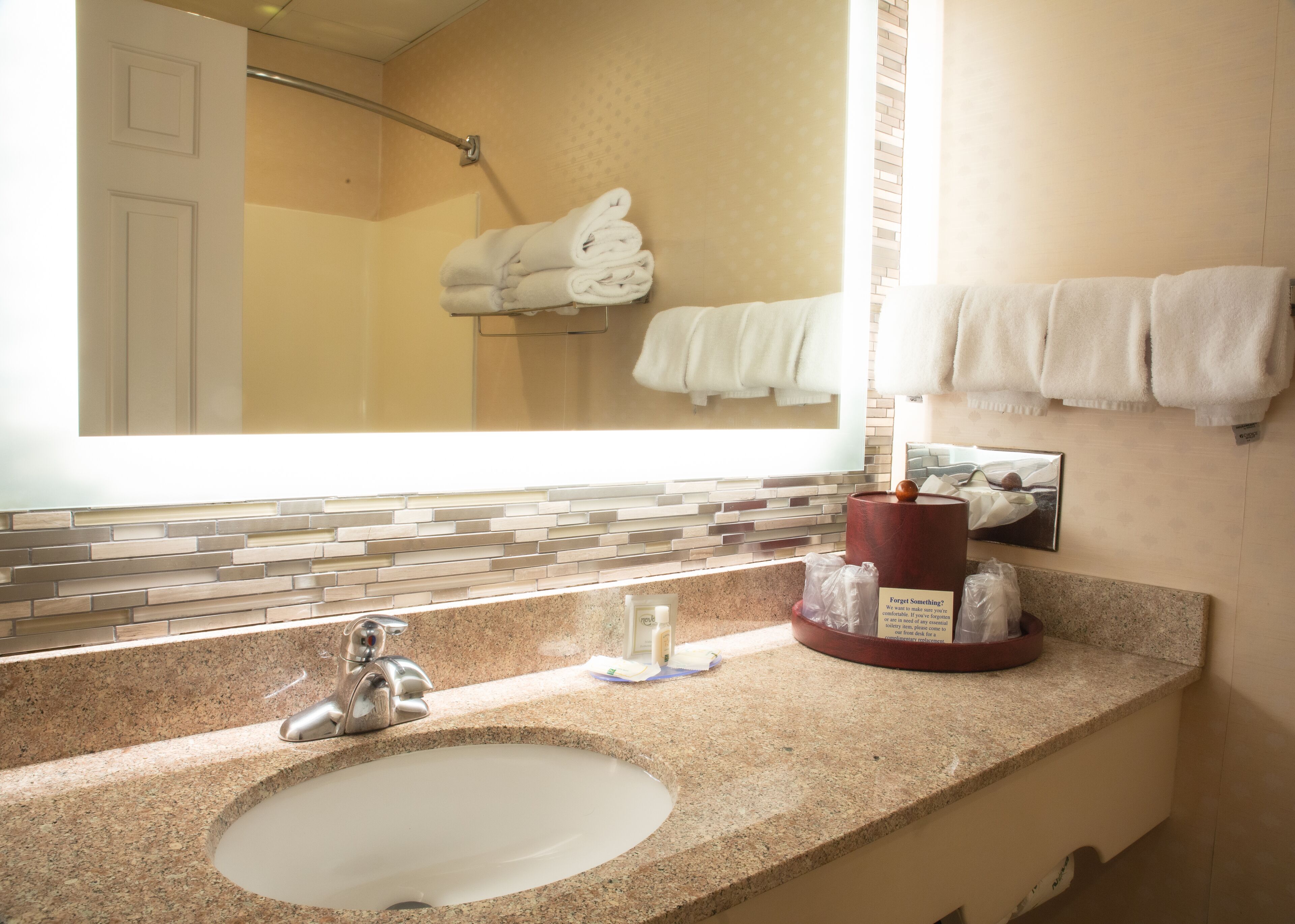 A bathroom with a granite countertop sink, a mirror, a towel rack, and a shower area.