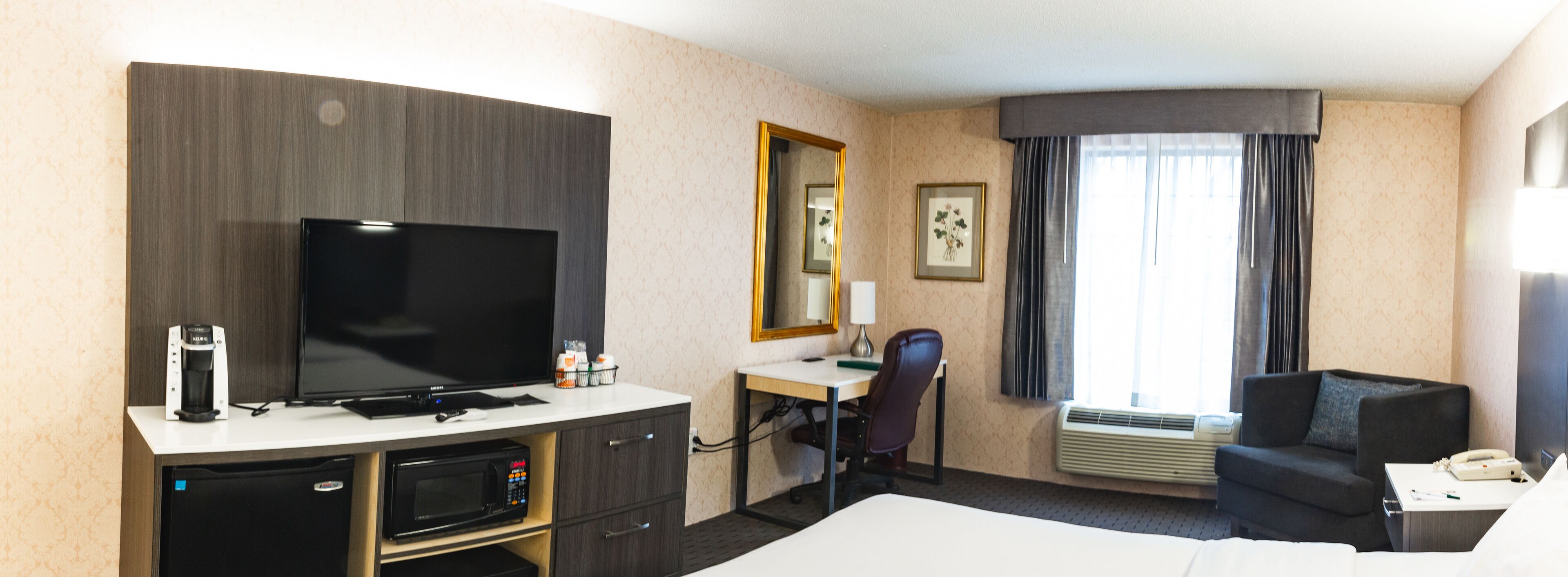 Quarto de hotel com televisão de tela plana, escrivaninha com cadeira, cama, sofá, micro-ondas e minibar.