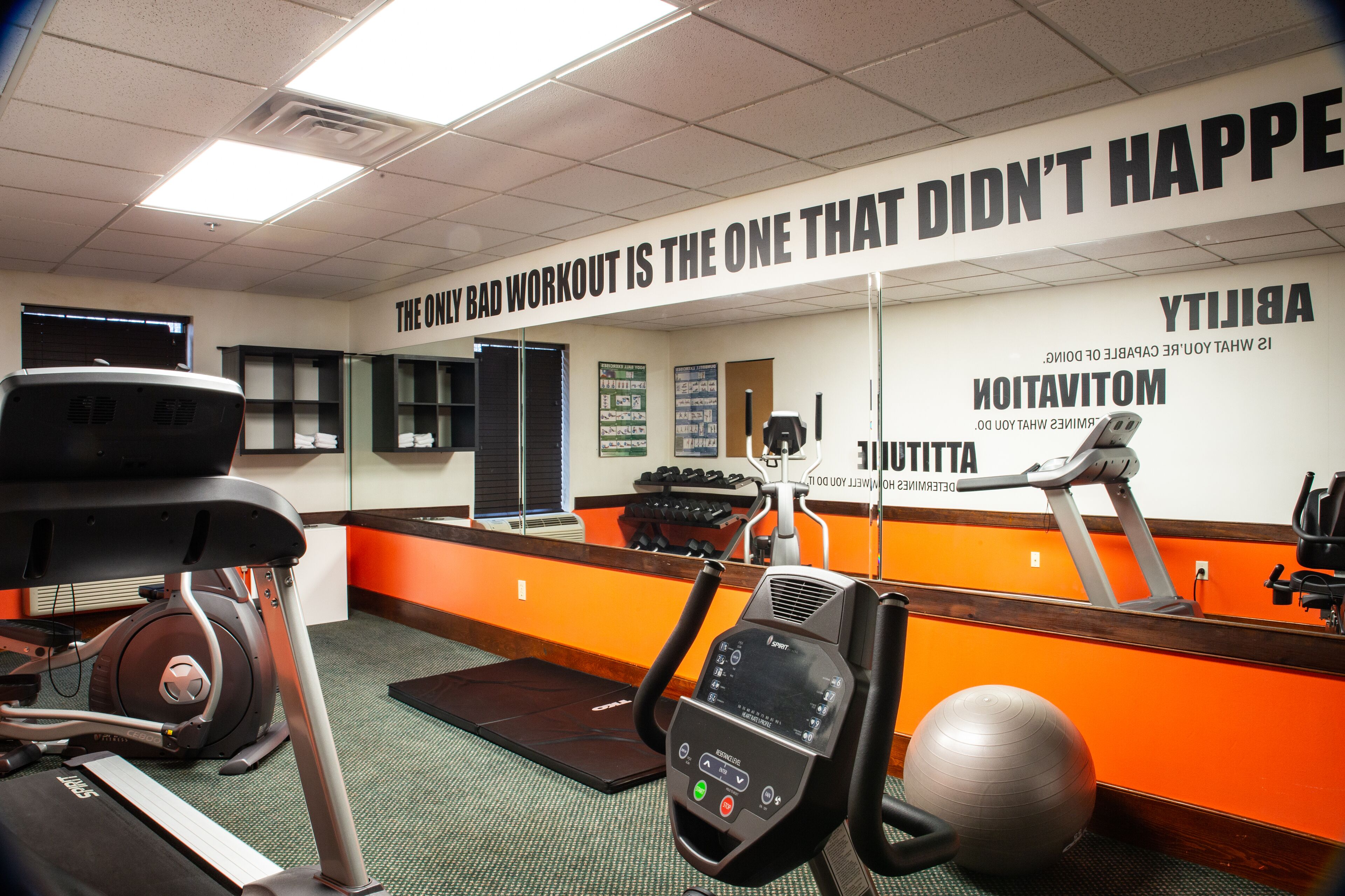 A gym with exercise equipment, motivational posters, and a mirrored wall.