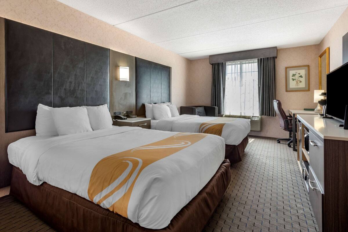 Une chambre d’hôtel avec deux lits, un bureau, une chaise, une télévision et une fenêtre avec des rideaux.