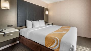 A hotel room with a large bed, a bedside table with a lamp, a telephone, and a wall-mounted light.