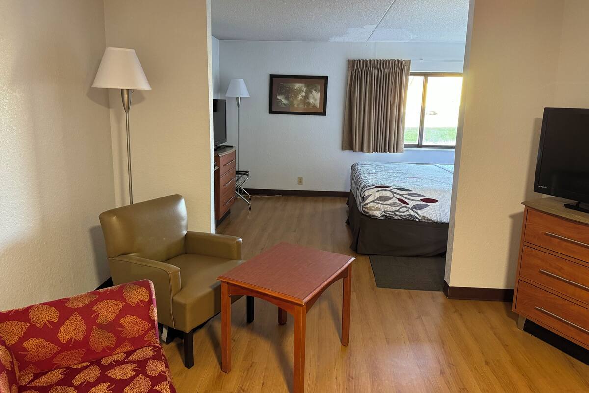 Habitación de hotel con cama, escritorio, silla, televisor y cómoda.