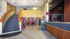 A hotel lobby with a staircase, a reception desk, and a seating area with a 'Free Wi-Fi' sign. - Sycamore Suites (Elyria)