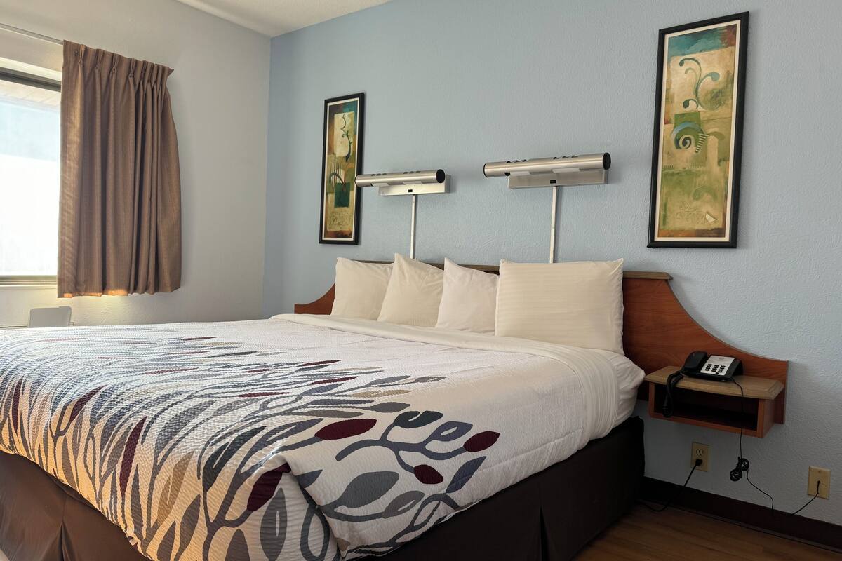 Una habitación de hotel con una cama grande, una mesita de noche con teléfono y dos lámparas de pared.