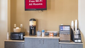 A kitchenette with a coffee maker, microwave, and a beverage dispenser. A TV above displays "Free Wi-Fi All Rooms". - Sycamore Suites (Elyria)