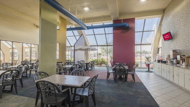 A spacious indoor dining area with multiple tables and chairs, large windows, and a visible kitchen area. - Sycamore Suites (Elyria)