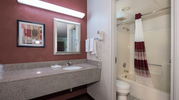 A bathroom with a granite countertop sink, a framed artwork, a hairdryer, and a shower with a striped curtain.