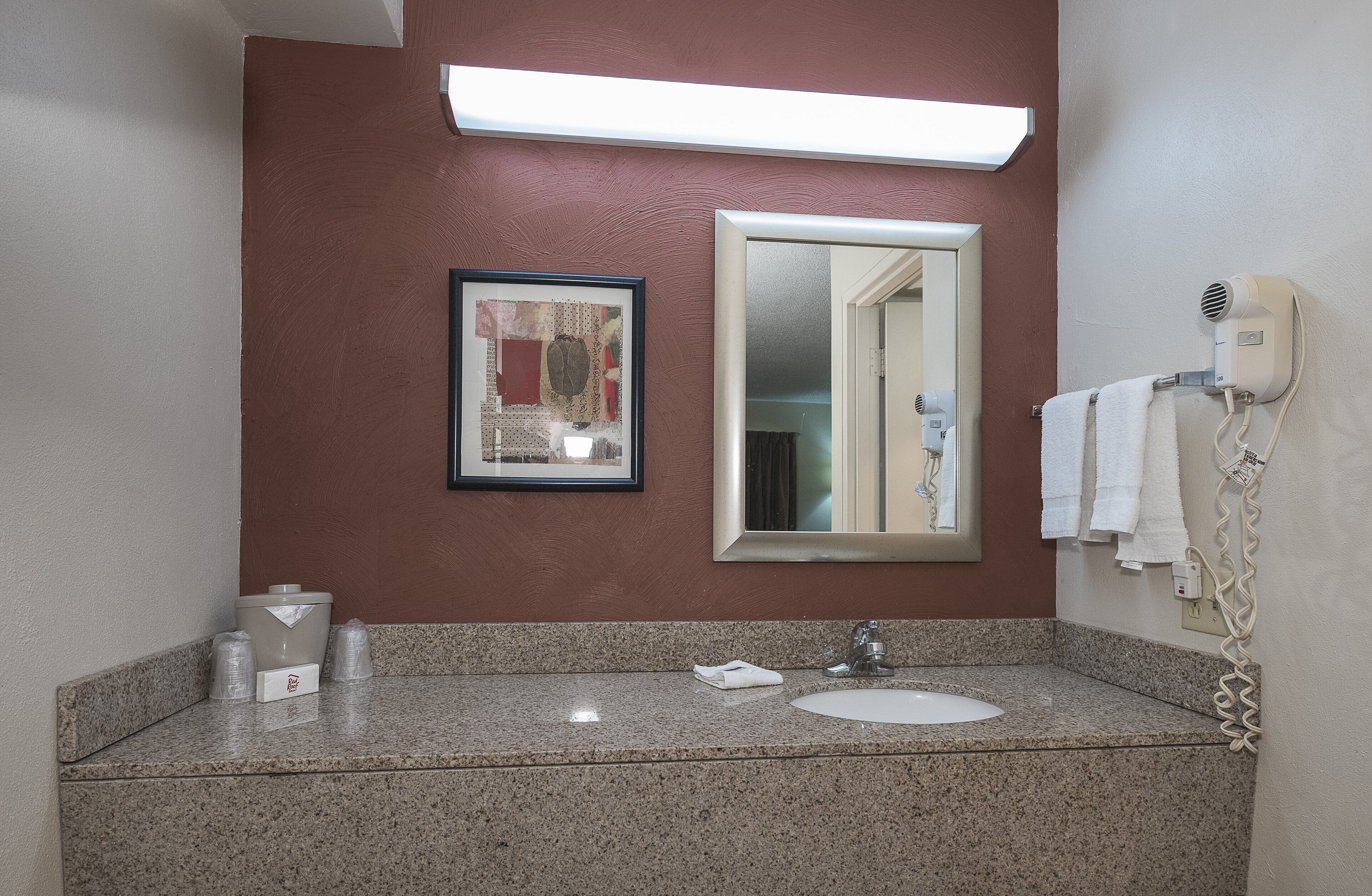 Un baño con encimera de granito, un lavabo, un espejo enmarco, un secador de pelo y un perchero para toallas.