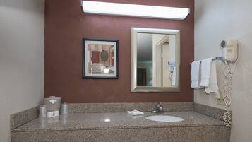 Un baño con encimera de granito, un lavabo, un espejo enmarco, un secador de pelo y un perchero para toallas.