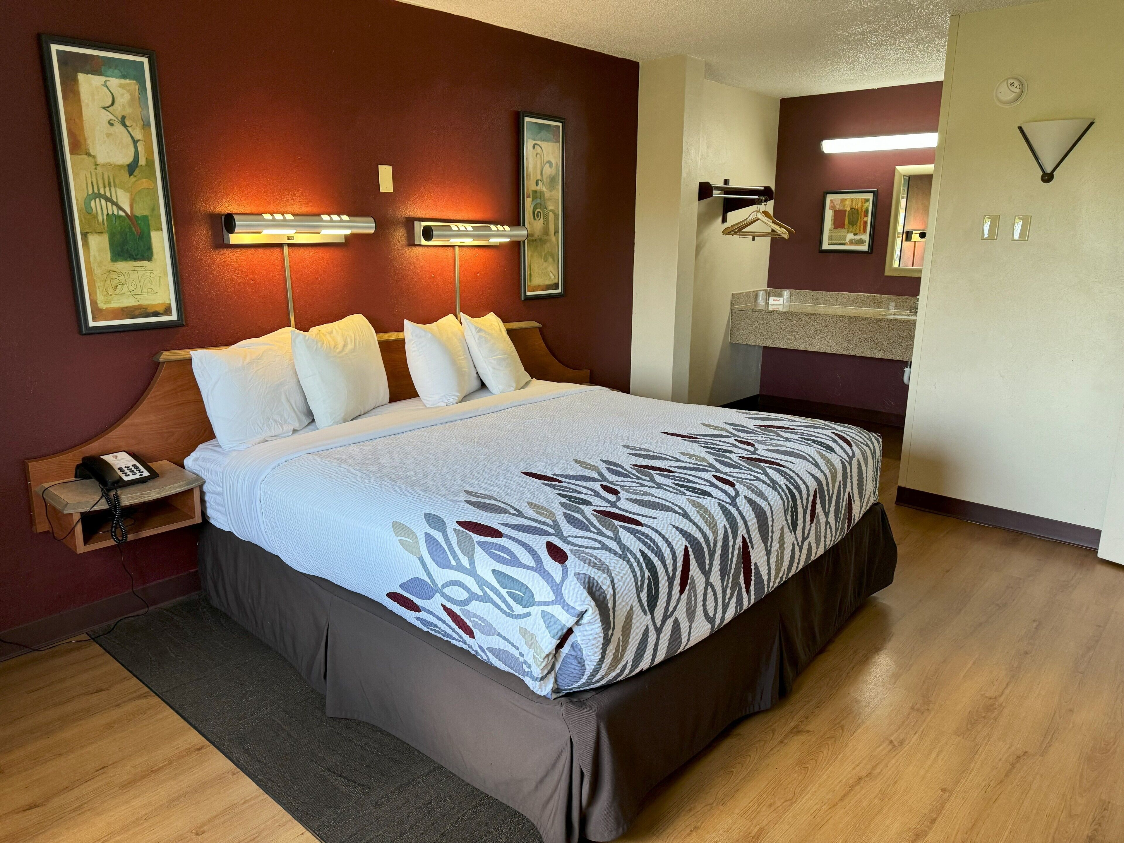 A neatly made bed with a patterned bedspread, a bedside phone, and a wall-mounted light fixture.