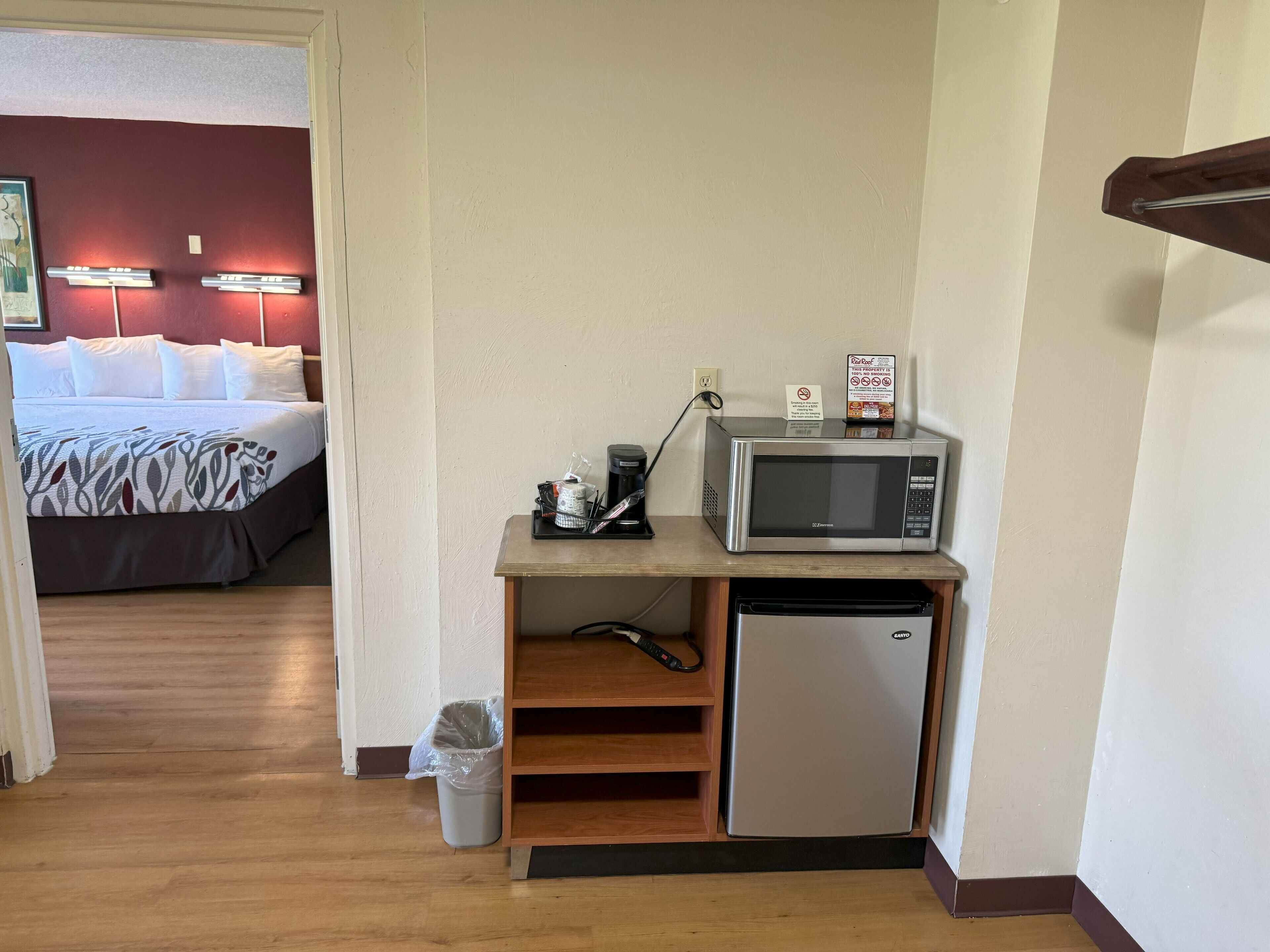 Ett litet, praktiskt kök med mikrovågsugn, kaffebryggare och kylskåp. En papperskorg står bredvid arbetsbänken.