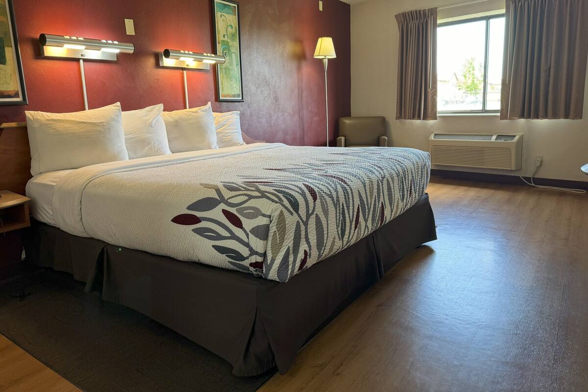 Habitación de hotel con una cama grande, un escritorio, una silla, una ventana con cortinas y un aire acondicionado montado en la pared.