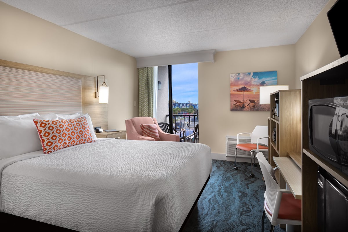 Une chambre d’hôtel avec un grand lit, un bureau avec une chaise, une télévision et un balcon avec vue.