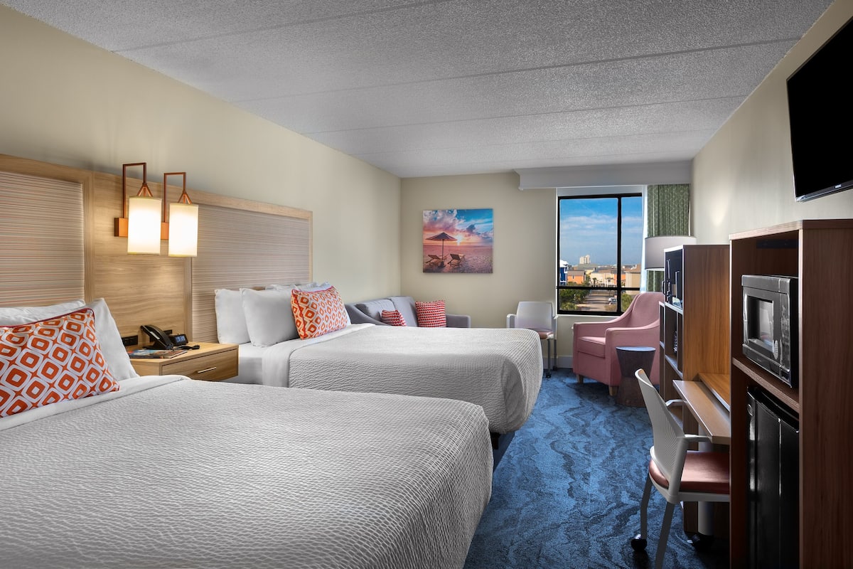 Une chambre d’hôtel avec deux lits, un bureau, une chaise, une télévision et une grande fenêtre donnant sur la ville.