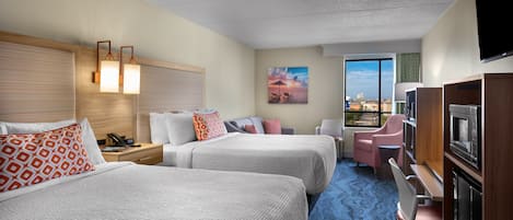 Une chambre d’hôtel avec deux lits, un bureau, une chaise, une télévision et une grande fenêtre donnant sur la ville.