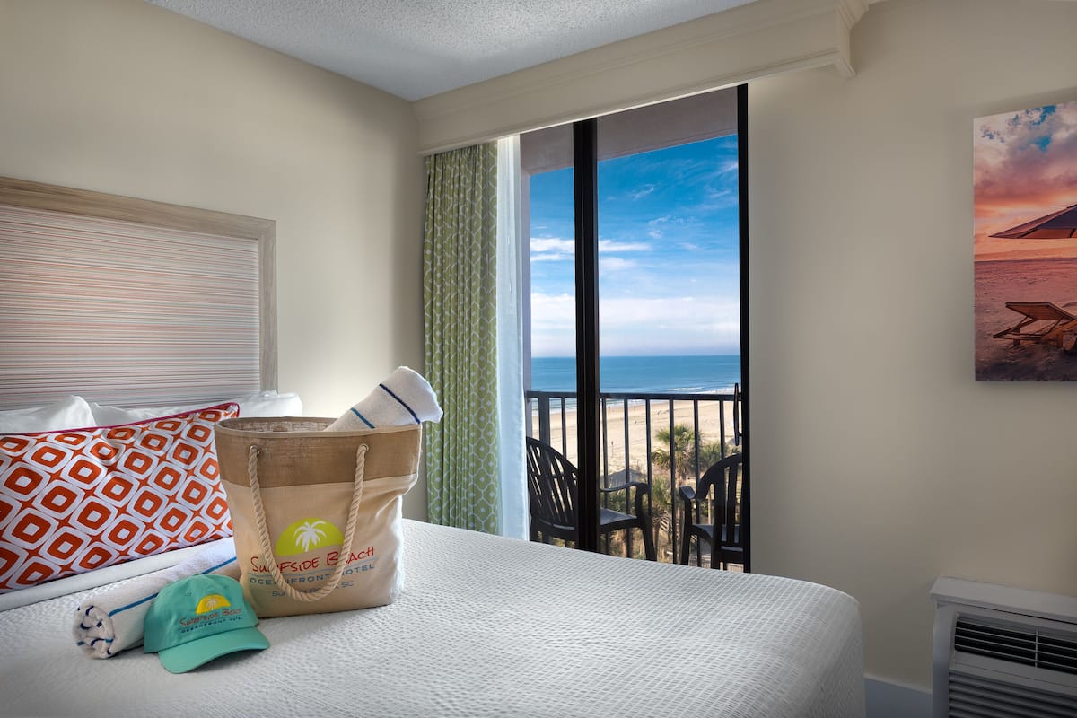 Une chambre d’hôtel avec un lit, une vue sur la plage, une serviette de plage, un chapeau et un sac.
