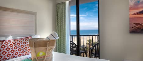 A hotel room with a bed, a view of the beach, a beach towel, a hat, and a bag.