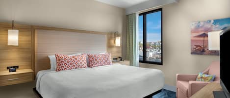 A hotel room with a large bed, a desk, a chair, a window with a city view, and a painting on the wall.