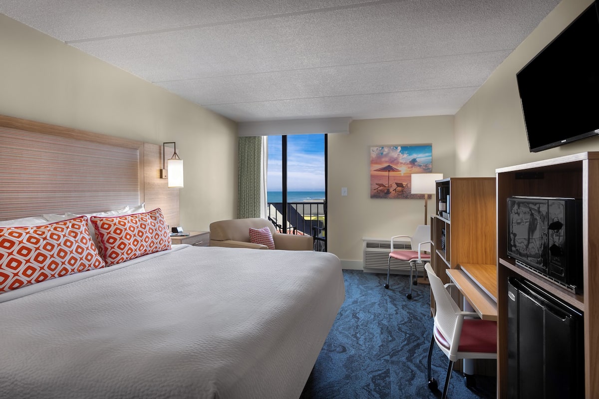 Une chambre d’hôtel avec un grand lit, un bureau, une télévision et une vue sur l’océan.