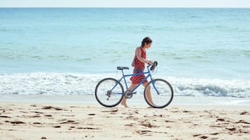 Une personne qui pousse un vélo sur une plage de sable, avec l’océan en arrière-plan.