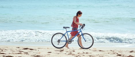 Une personne qui pousse un vélo sur une plage de sable, avec l’océan en arrière-plan.