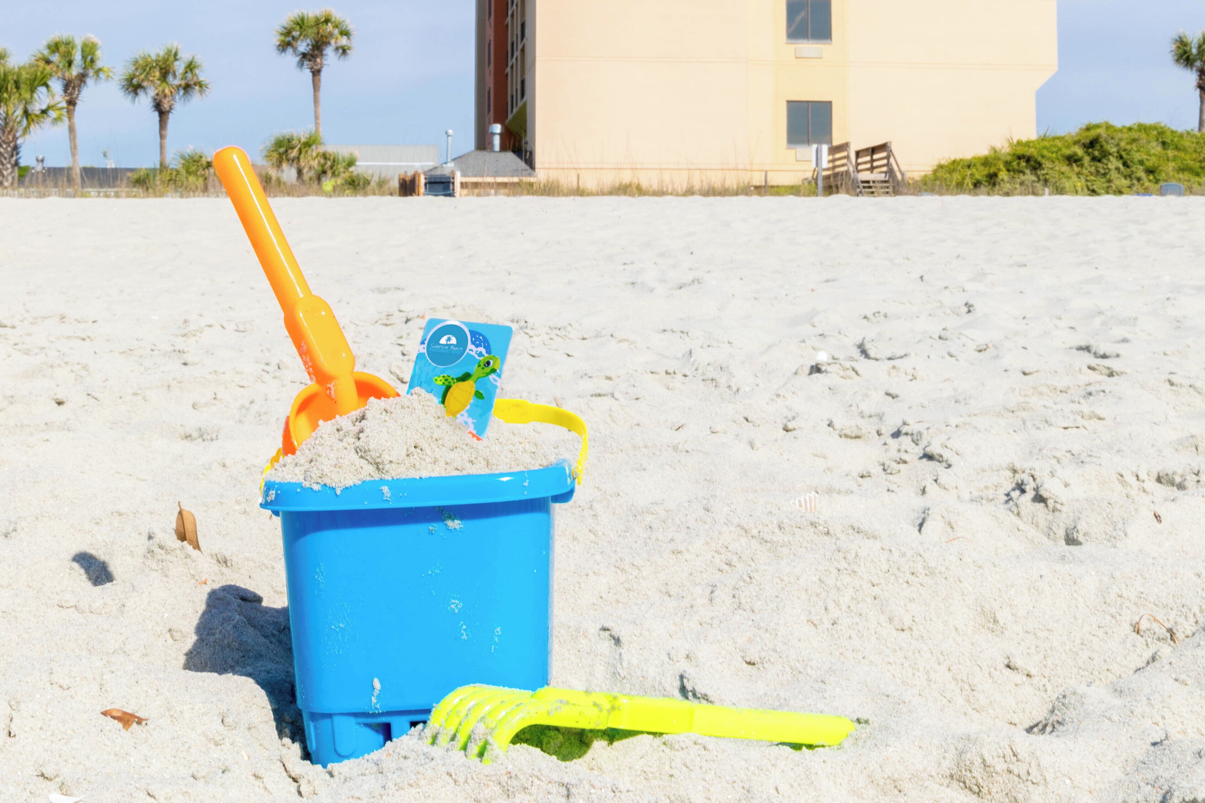 Un cubo azul de arena con una pala y un juguete en una playa arenosa.