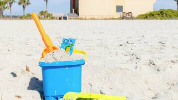 Un cubo azul de arena con una pala y un juguete en una playa arenosa.