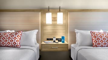 A hotel room with two beds, a bedside table with a lamp, a phone, and a water bottle.