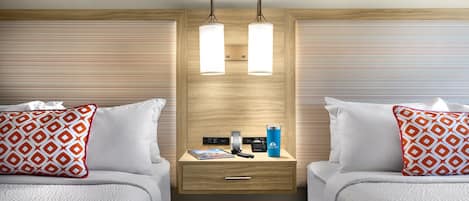 A hotel room with two beds, a bedside table with a lamp, a phone, and a water bottle.