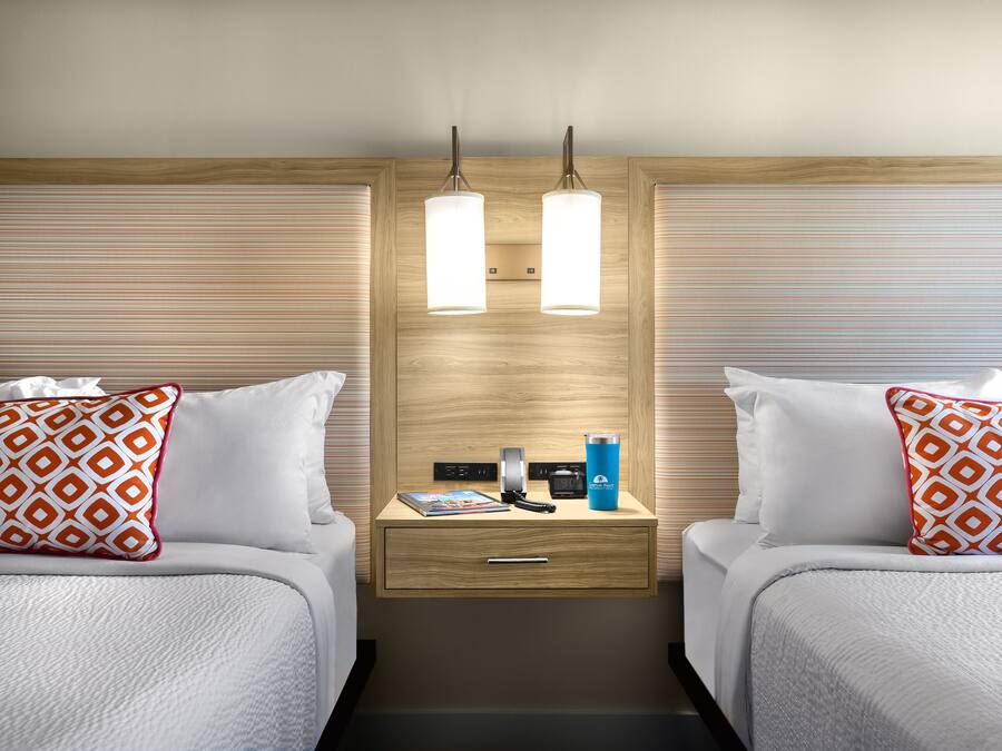A hotel room with two beds, a bedside table with a lamp, a phone, and a water bottle.