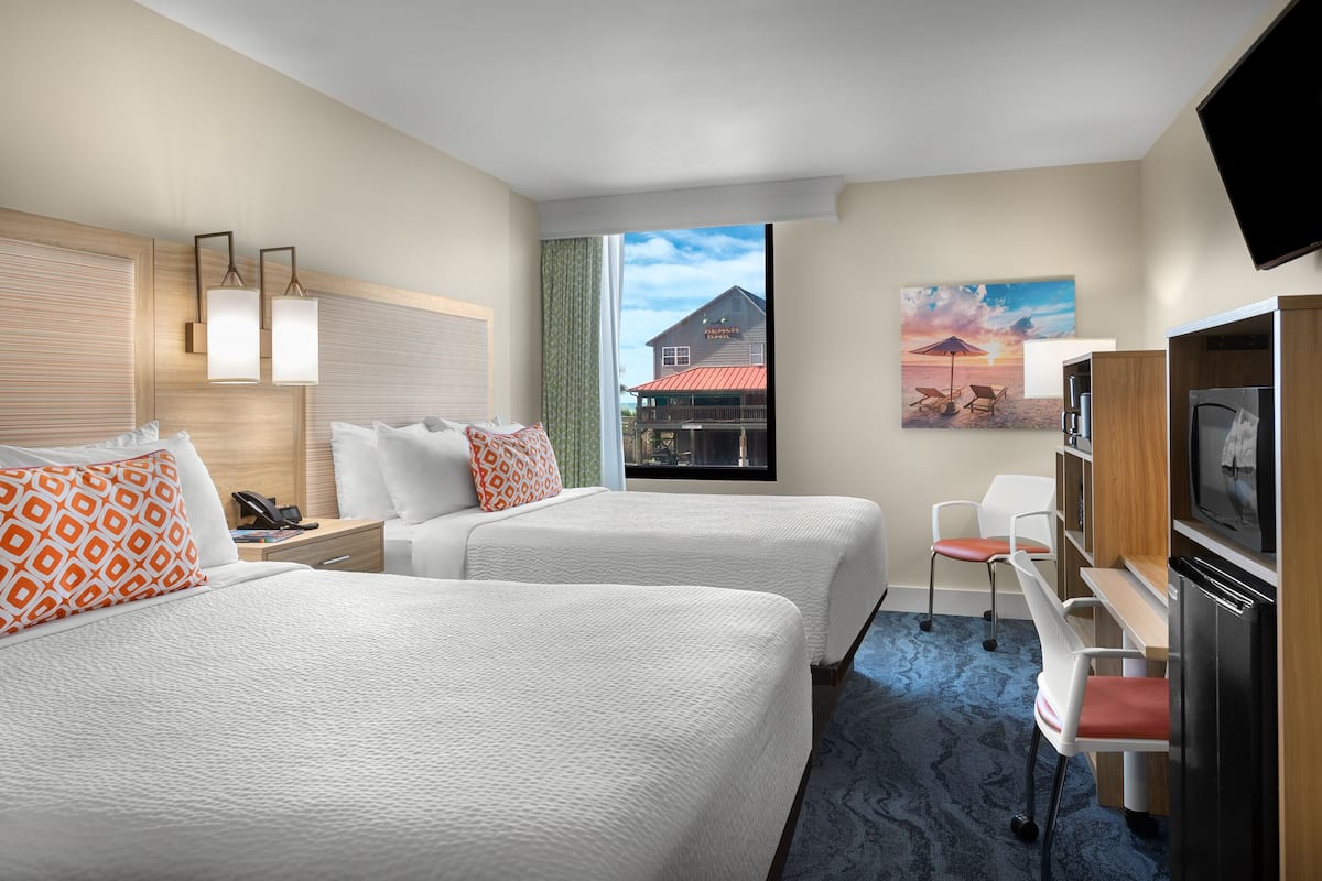 Une chambre d’hôtel avec deux lits, un bureau, une télévision et une vue sur un bâtiment situé à l’extérieur.