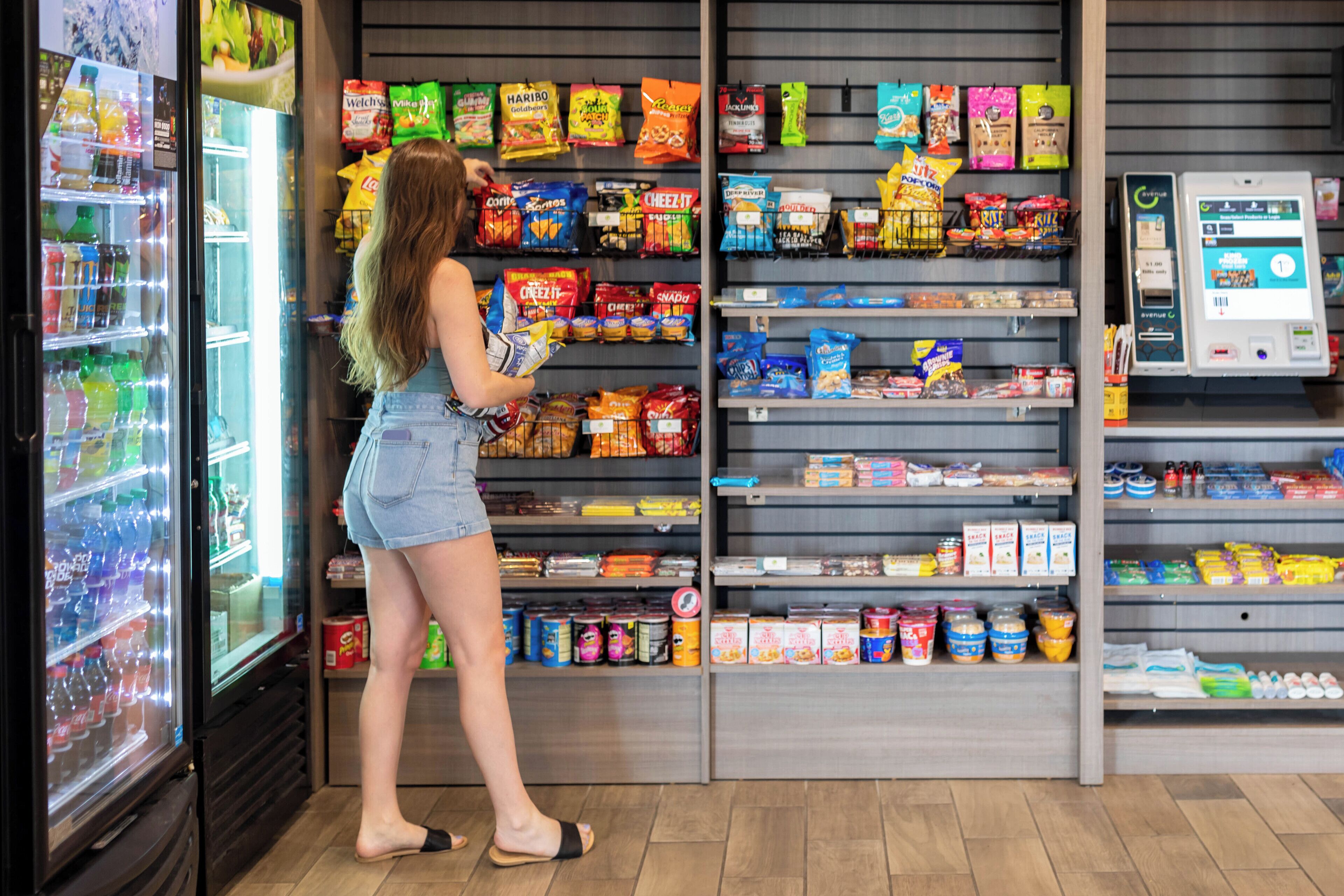 A woman shopping in a grocery store aisle with shelves stocked with snacks and beverages.