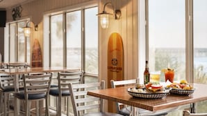 A restaurant with wooden tables and chairs, a Longboard beer bottle, a beer bottle, a glass of beer, a Bloody Mary, and a basket of nachos.