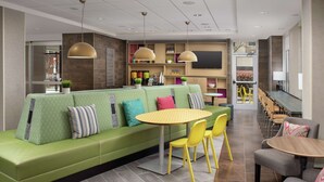 A modern lounge area with a green sofa, yellow chairs, and a round table. - Home2 Suites by Hilton Atlanta Midtown (Atlanta)