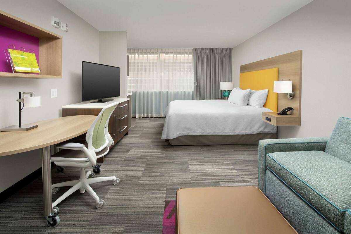 A hotel room with a bed, desk, chair, TV, and a sofa.