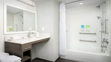 Un baño moderno con lavamanos, espejo y zona de ducha blancos.