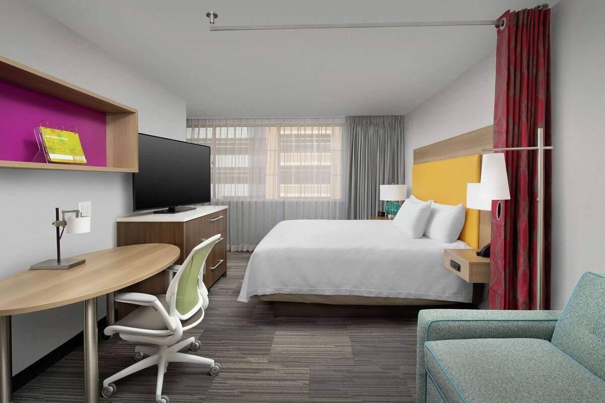 A hotel room with a bed, desk, chair, TV, and a small sofa.