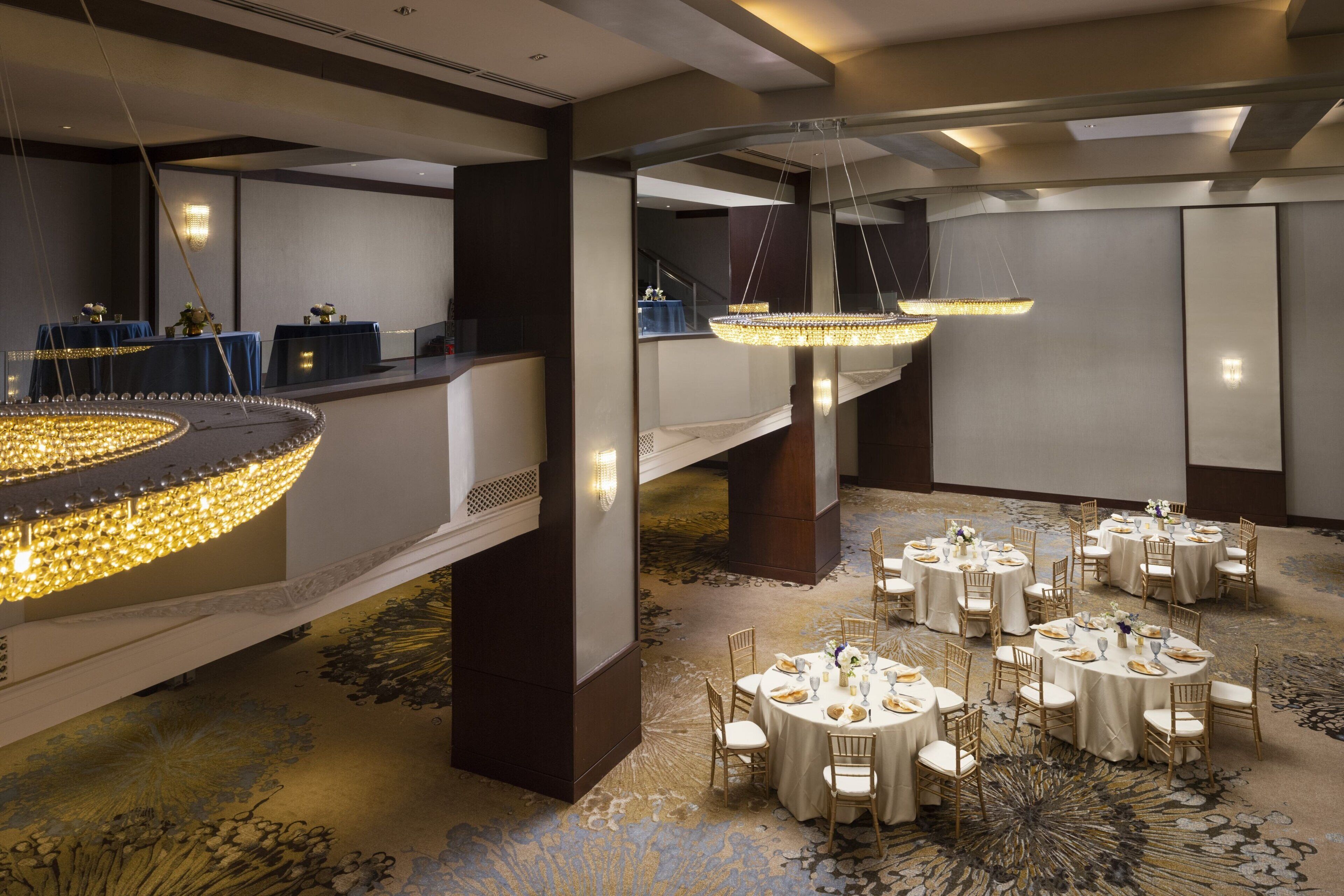 A banquet hall with round tables, chandeliers, and a carpeted floor.
