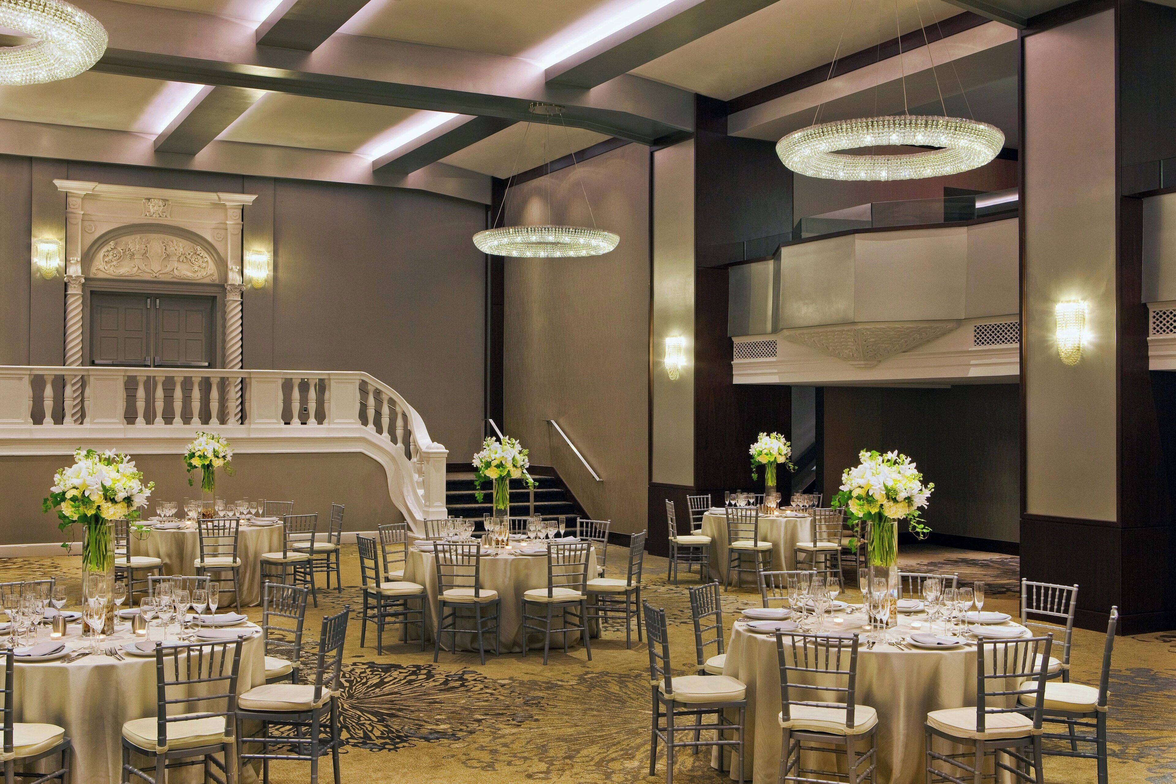 A banquet hall with round tables, chairs, and chandeliers.