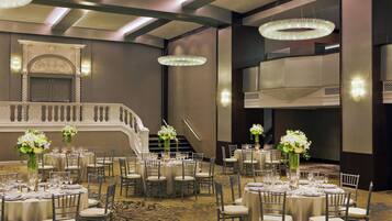 A banquet hall with round tables, chairs, and chandeliers.