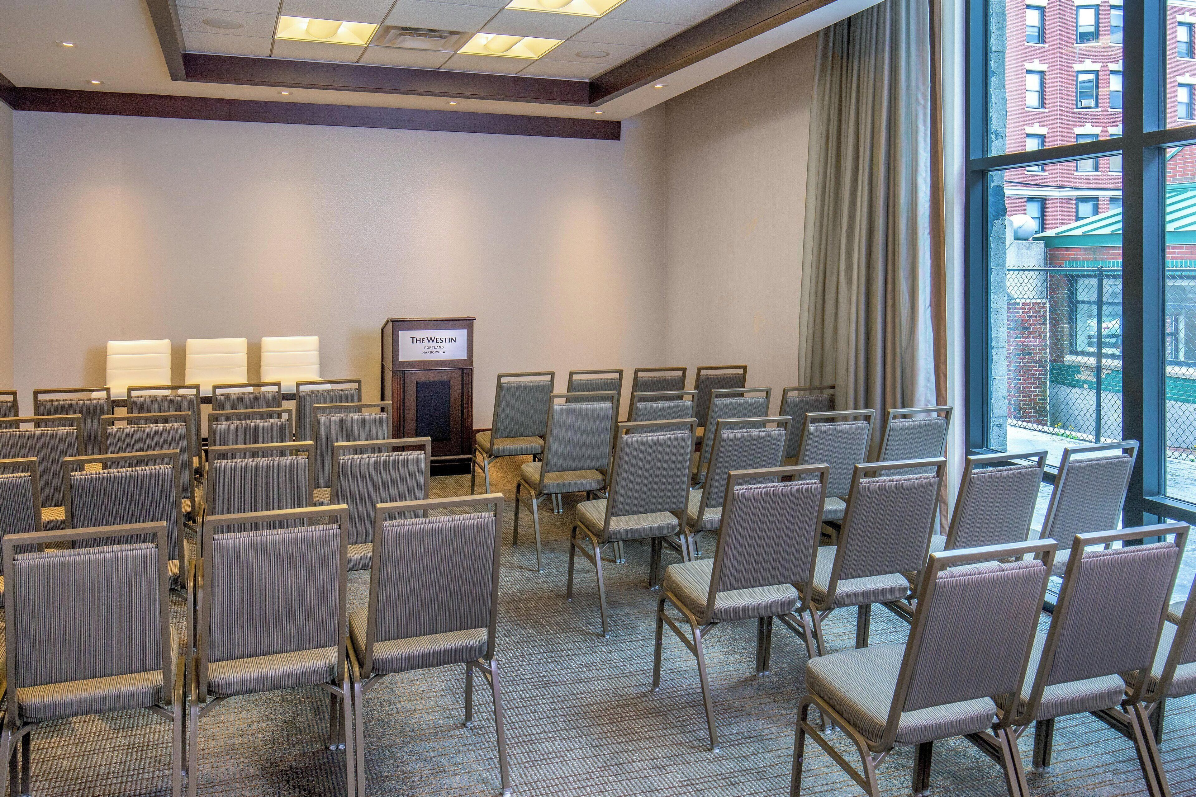 A conference room with rows of chairs, a podium, and a view of the city through large windows.