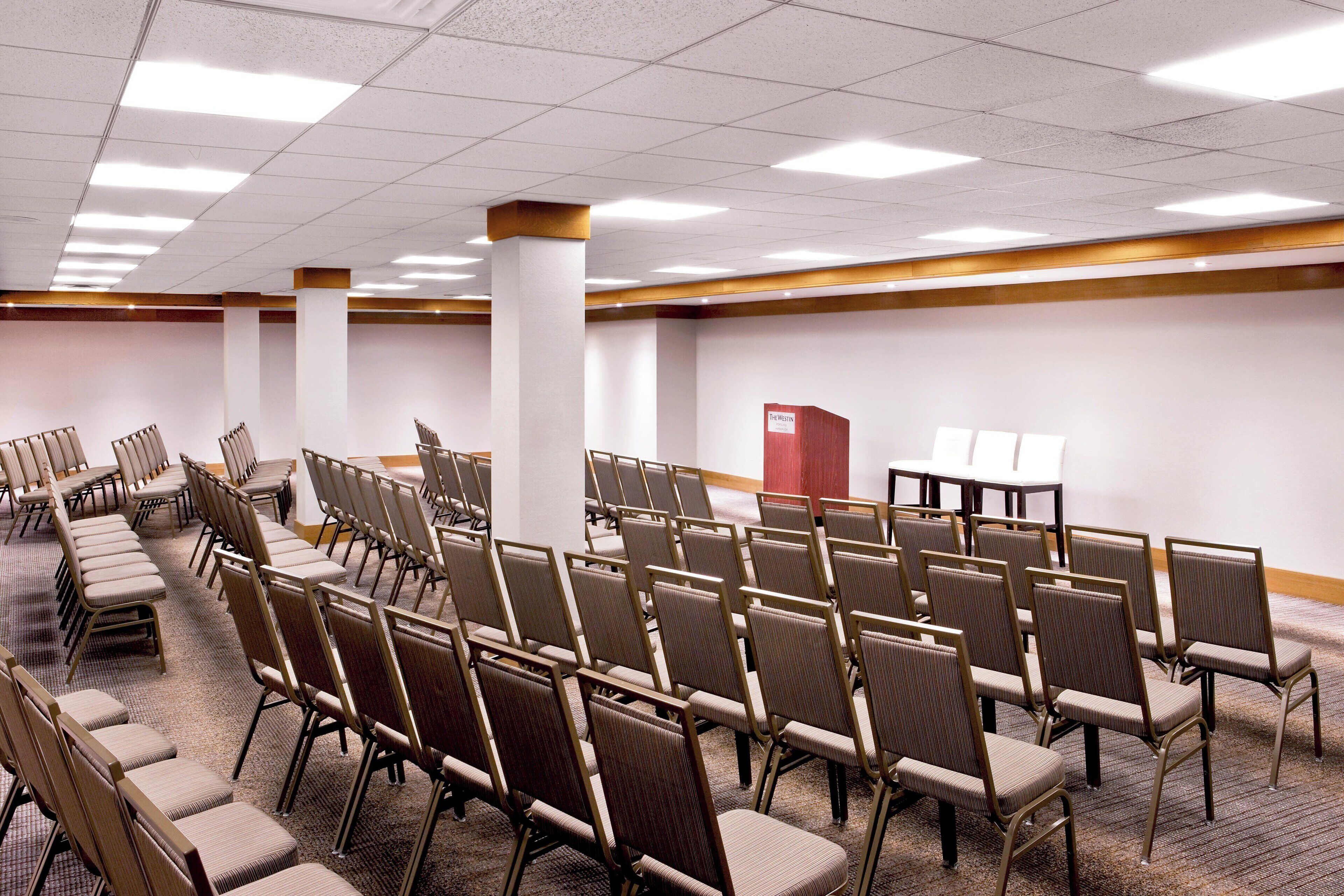 A conference room with rows of chairs, a podium, and a carpeted floor.